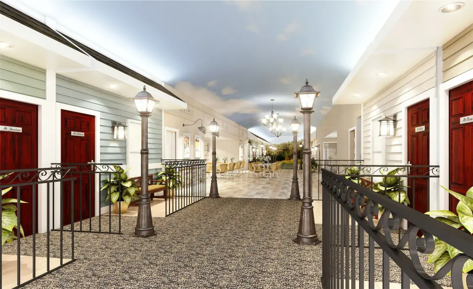Indoor corridor mimicking a street, with red doors, street lamps, plants, and a blue sky ceiling. Bright and welcoming atmosphere with a café visible.
